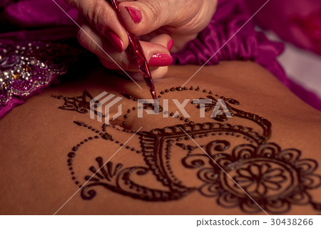 Mehendi artist paints an ornament of henna on an e 30438266
