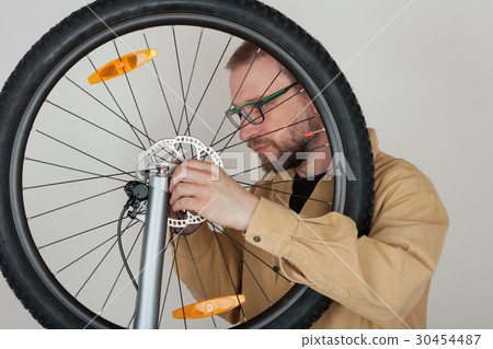 Bearded man screws the front wheel on bicycle. 30454487