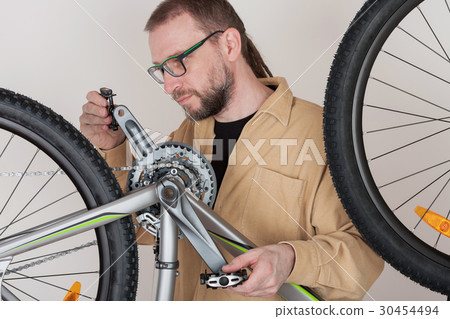 Bearded man screws the pedals on the mtb bicycle. 30454494