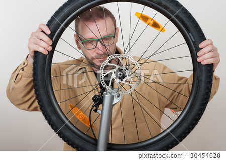 Bearded man puts the front wheel on the bicycle. 30454620