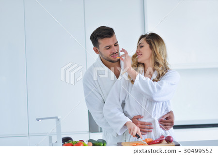 Happy couple cooking breakfast together in the Happy couple cooking breakfast together in the 30499552