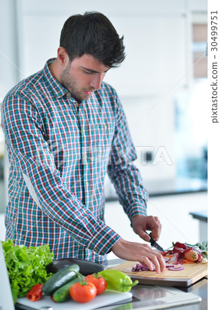Handsome man cooking at home preparing salad in 30499751