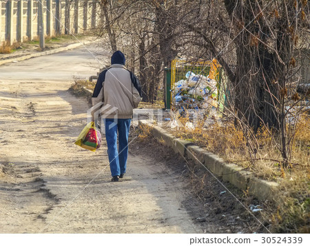 Man carries bag of trash to a dumpster 30524339
