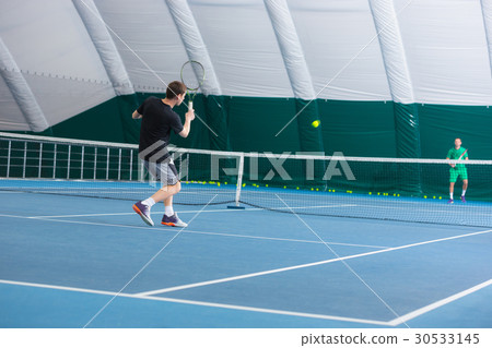 The young man in a closed tennis court with ball 30533145