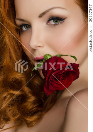 woman with long red hair holds rose in her mouth 30537547