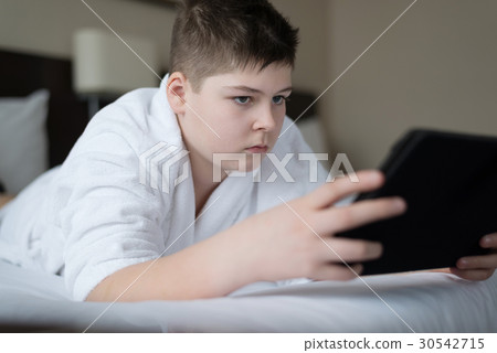 Boy in bathrobe Uses tablet in hotel room 30542715