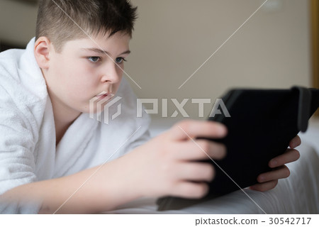 Boy in bathrobe Uses tablet in hotel room 30542717