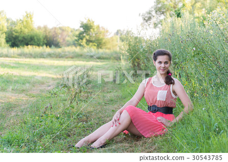 girl in red dress is sitting on the grass 30543785