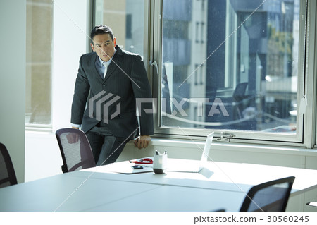 the businessman is leaning against the glass window. 30560245