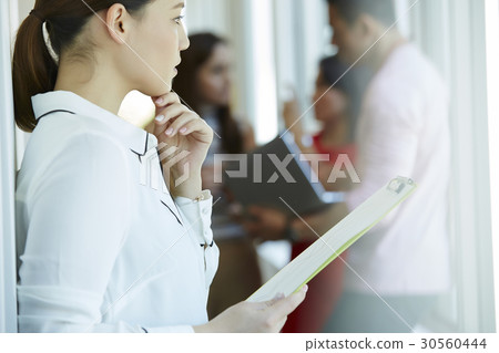 A businesswoman is holding documents and looking at something. A businesswoman is holding documents and looking at something. 30560444