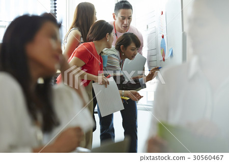 A woman is writing on a board in a group discussion A woman is writing on a board in a group discussion 30560467