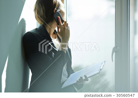 a businesswoman is talking on phone and looking outside a businesswoman is talking on phone and looking outside 30560547