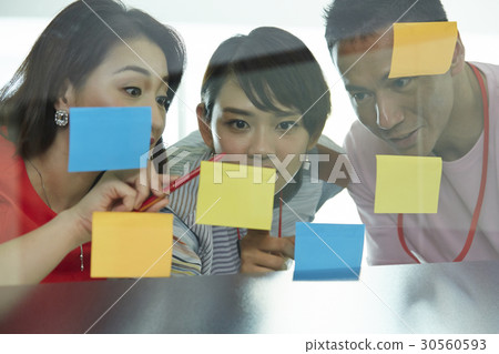 Three colleagues are discussing new ideas on sticky notes. Three colleagues are discussing new ideas on sticky notes. 30560593
