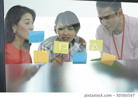Three colleagues are looking and discussing new ideas on sticky notes. Three colleagues are looking and discussing new ideas on sticky notes. 30560597