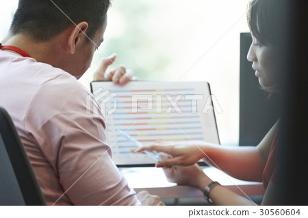 Two colleagues are reading a document in an office. 30560604