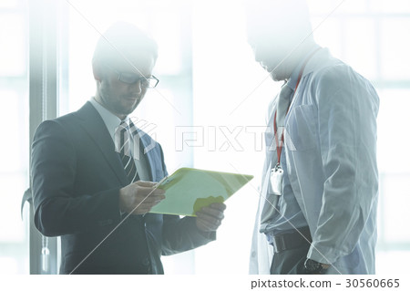 A doctor and an administrator are discussing in hospital. 30560665