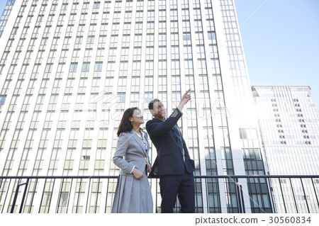 a man and a woman are looking at something beside a building 30560834