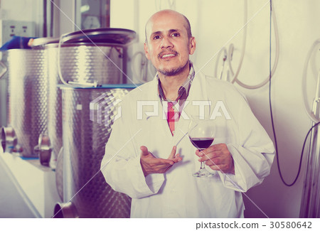 mature man in white coat having glass with wine in hands at fact 30580642