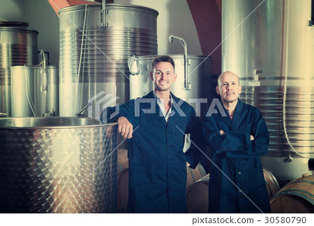 Two happy men in uniforms standing in winery fermentation compartment Two happy men in uniforms standing in winery fermentation compartment 30580790