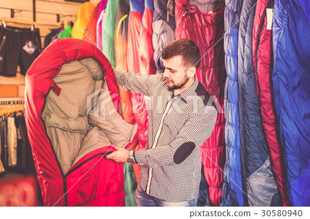 Young male customer choosing new sleeping bag Young male customer choosing new sleeping bag 30580940