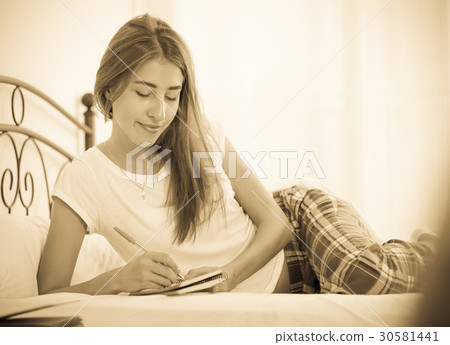Smiling girl making shopping list in bedroom 30581441