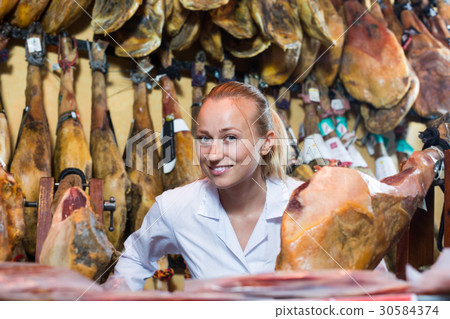 Closeup of cheerful woman seller showing iberian jamon 30584374