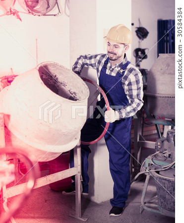 Young smiling guy using concrete mixer at workshop 30584384