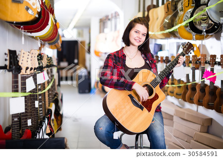 Nice girl examining various acoustic guitars 30584591