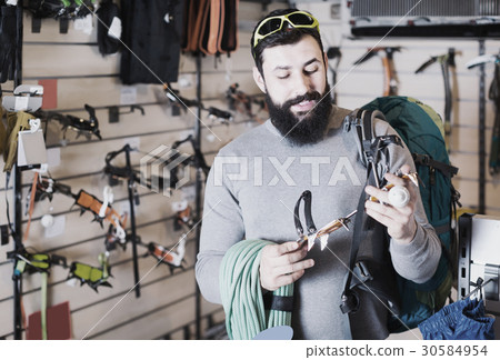 cheerful male customer examining climbing equipment in sports equipment store 30584954