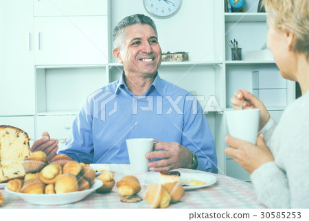 Mature couple have an afternoon snack with fresh muffins and cake Mature couple have an afternoon snack with fresh muffins and cake 30585253