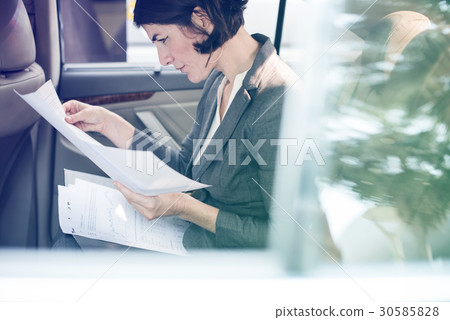 Businesswoman reading documents on backseat of the car 30585828