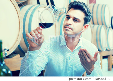 Positive male expert holding glass of red wine in shop 30586109
