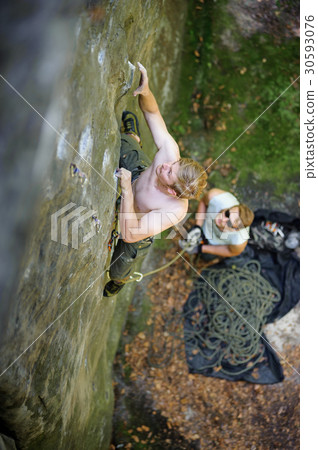 Muscular rock climber climbs on cliff with rope 30593076