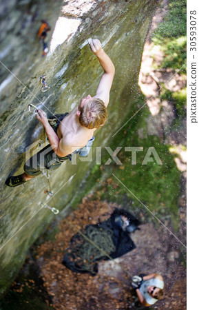 Muscular rock climber climbs on cliff with rope 30593078