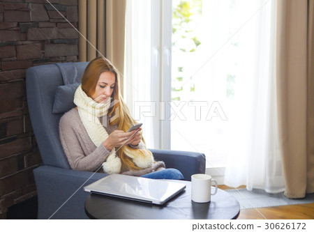 Woman in armchair writing a text message on phone 30626172