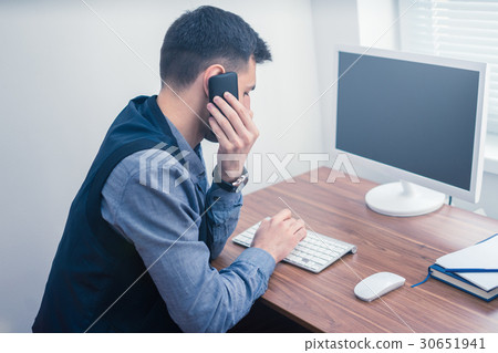 Man in office on telephone using computer and Man in office on telephone using computer and 30651941