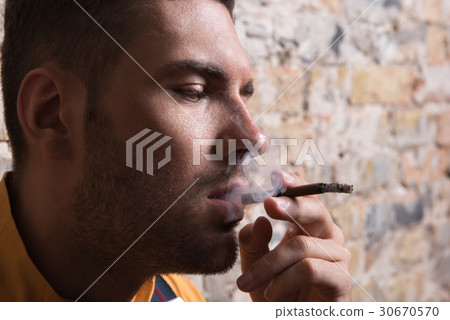 Young melancholic man exhaling cigarette smoke 30670570