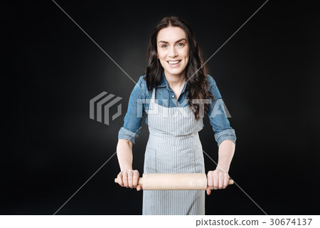 Positive pretty female holding rolling-pin in both 30674137
