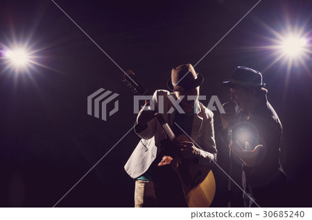 Musician Duo band hand holding the microphone and singing a song and playing the guitar on black background with spot light and lens flare, musical concept 30685240