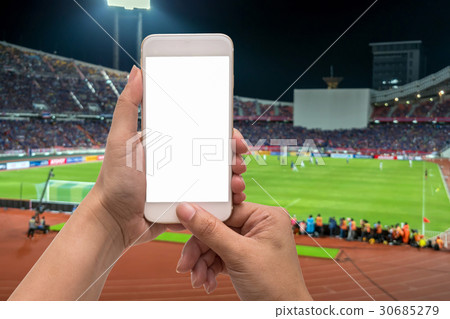 Female hand holding mobile smart phone touch screen on blurred of action photographer taking photo at player in Abstract blurred photo of soccer stadium, sport background concept 30685279