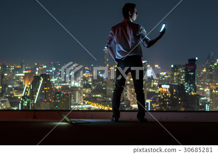 Asian businessman standing and using the smart mobile phone over the cityscape background at night time, Business success and technology concept Asian businessman standing and using the smart mobile phone over the cityscape background at night time, Business success and technology concept 30685281