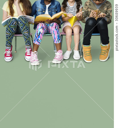 Diverse group of kids sitting in a row reading books 30689939