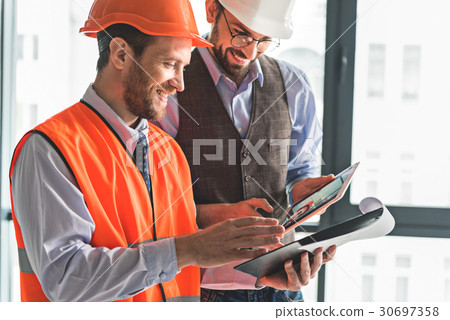 Joyful smiling builders checking documents Joyful smiling builders checking documents 30697358