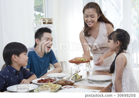 Mother is bringing food to her family at the dining table. Mother is bringing food to her family at the dining table. 30698208