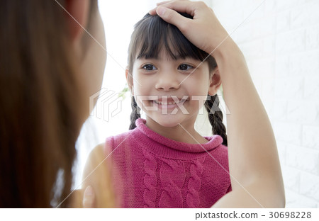Mother is touching the head of the little daughter. 30698228