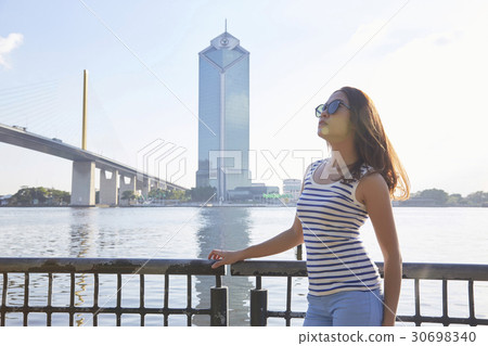 A girl with glasses is standing on a riverside and looking at the sky. 30698340