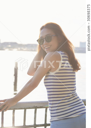 A girl with sunglasses is standing, looking back and smiling. 30698375