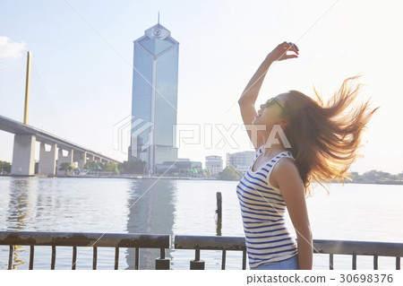 A girl is standing on a riverside, rising her arm and looking up. 30698376