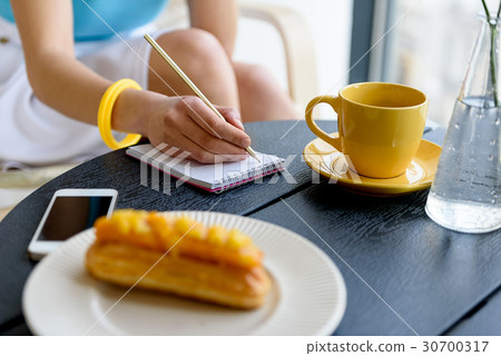 Elegant lady sitting at table and writing down her 30700317