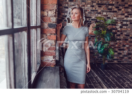 Beautiful blonde woman in a gray dress is standing Beautiful blonde woman in a gray dress is standing 30704119